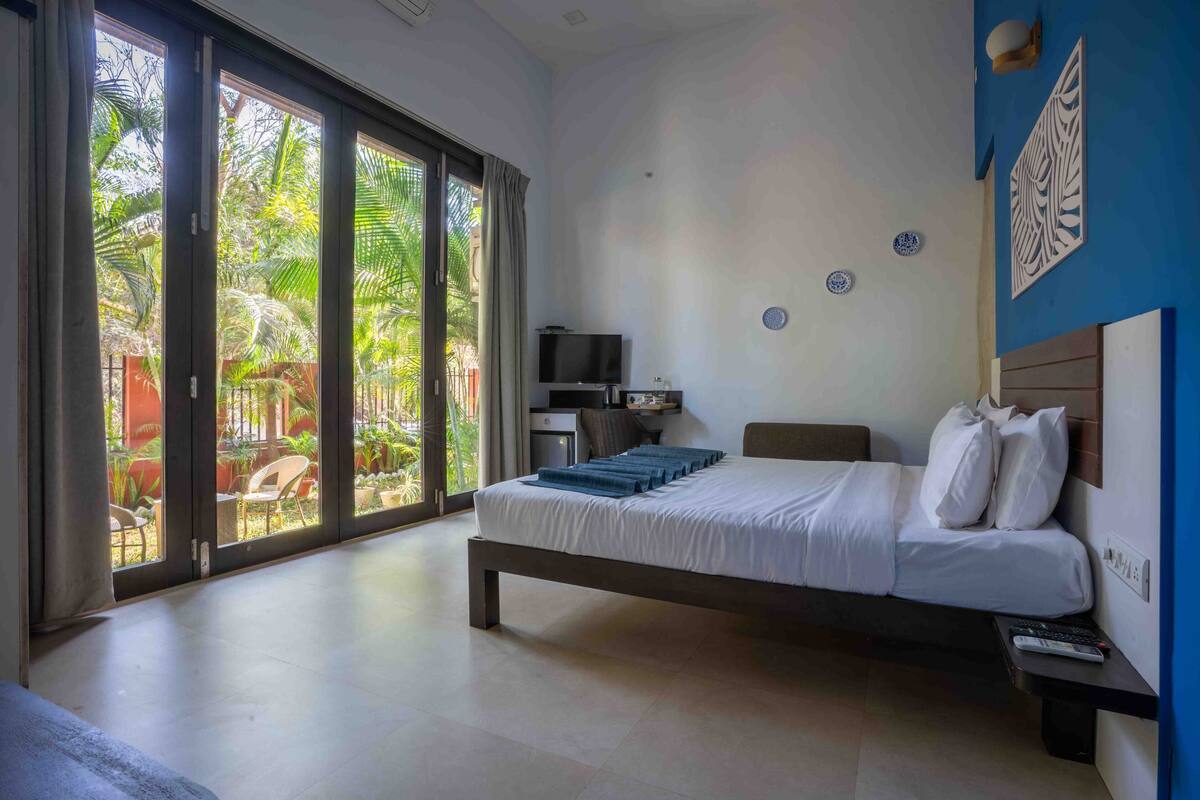 A hotel room with a bed, a TV, a desk, and a view of the outdoors.