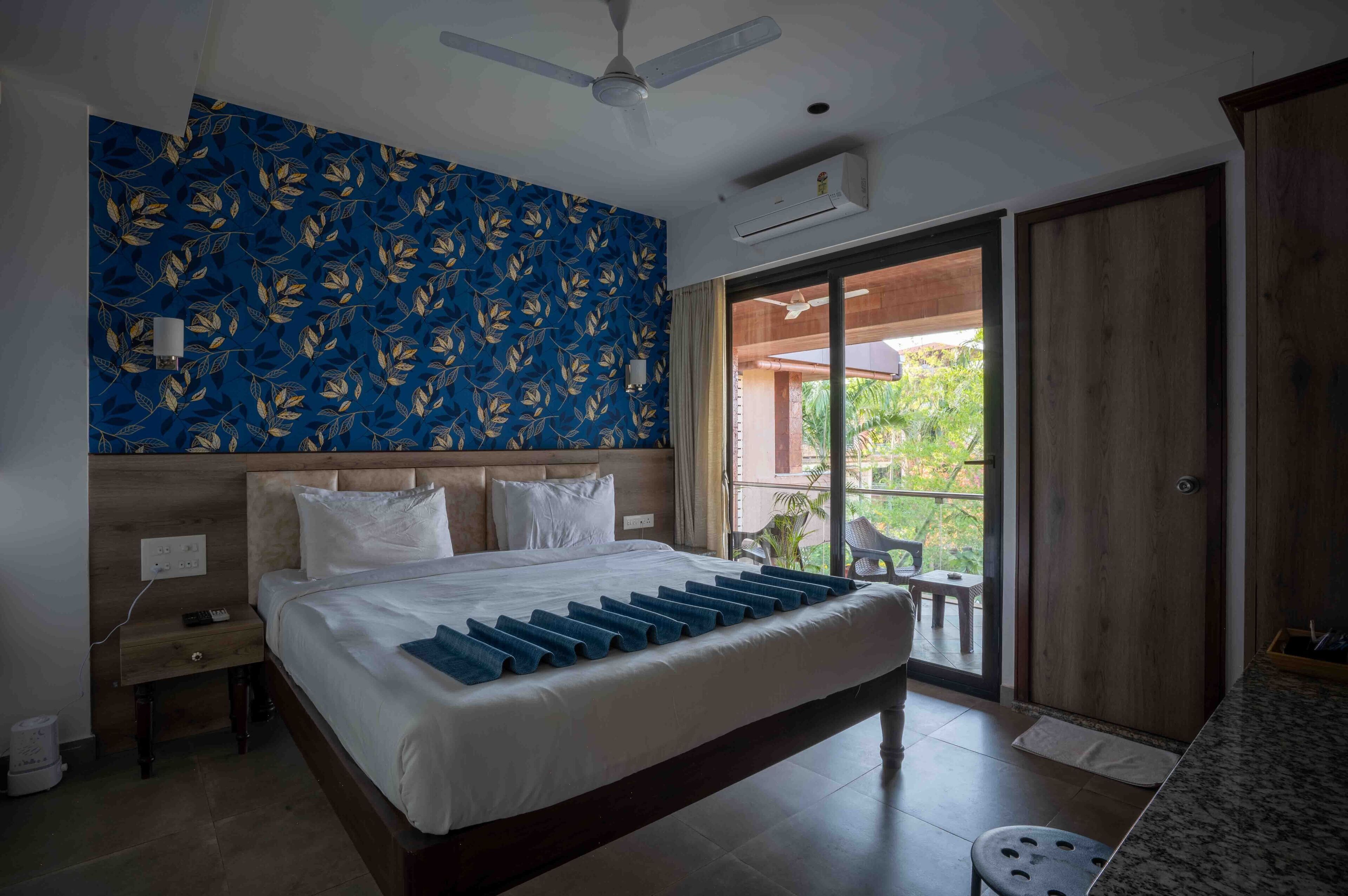 A bedroom with a bed, a nightstand, a ceiling fan, a window, and a sliding door leading to an outdoor area.