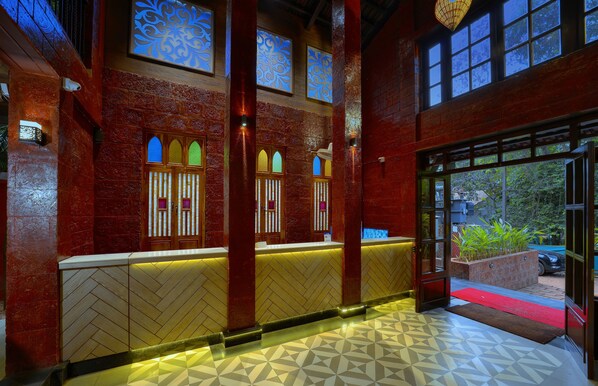 A reception area with a herringbone patterned floor, a reception desk, and a red carpet leading outside.