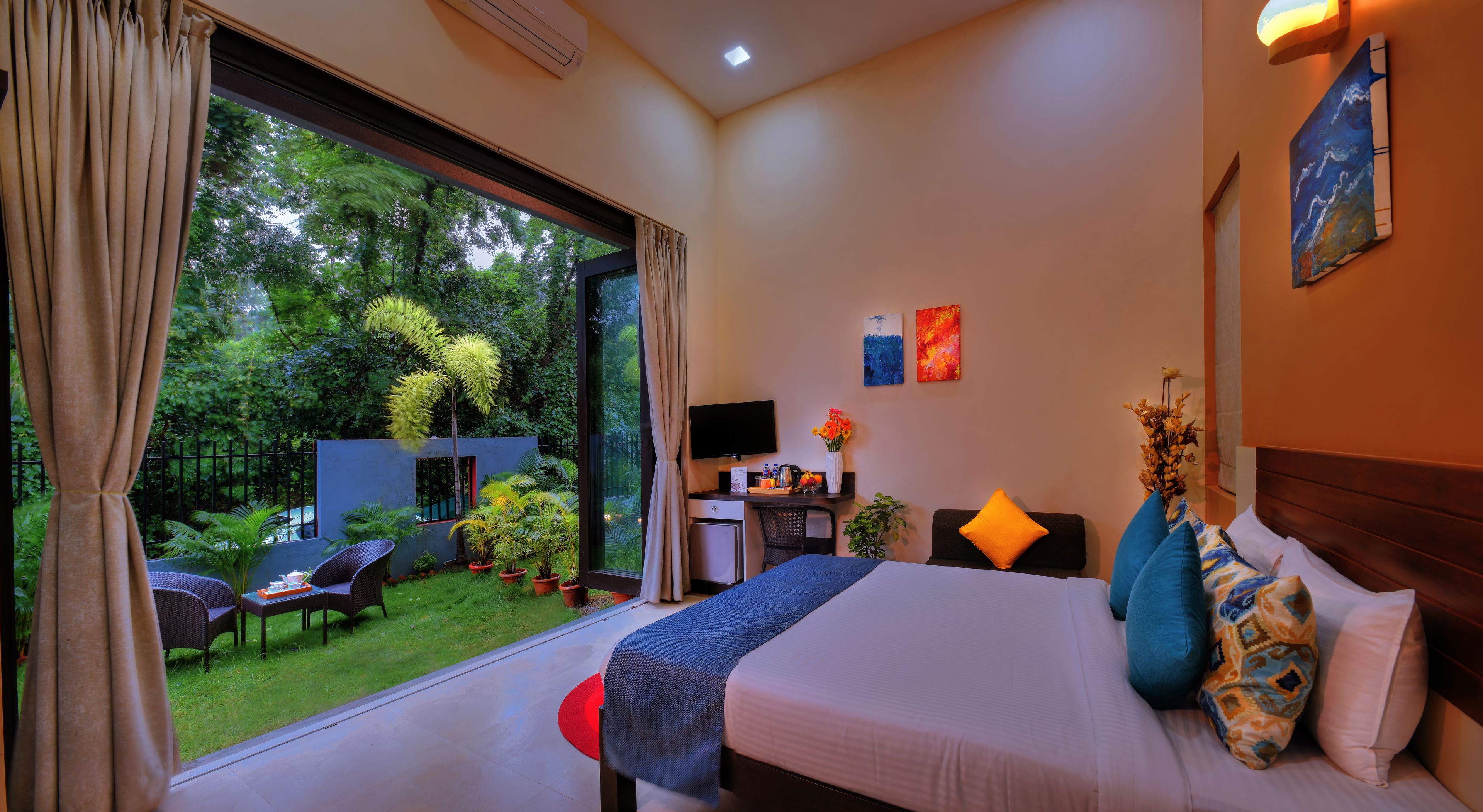 A hotel room with a large bed, a desk with a computer, a TV, and a view of a garden.