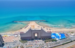 A large hotel with a central courtyard, a beach area, and a parking lot.