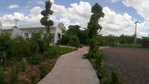 Un sendero que lleva a un edificio blanco con techo verde, rodeado de vegetación y una masa de agua.