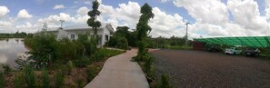 A pathway leading to a white building with a green roof, surrounded by greenery and a body of water. - Coffee&Homestay568 Branch 2 (Muang Suang)
