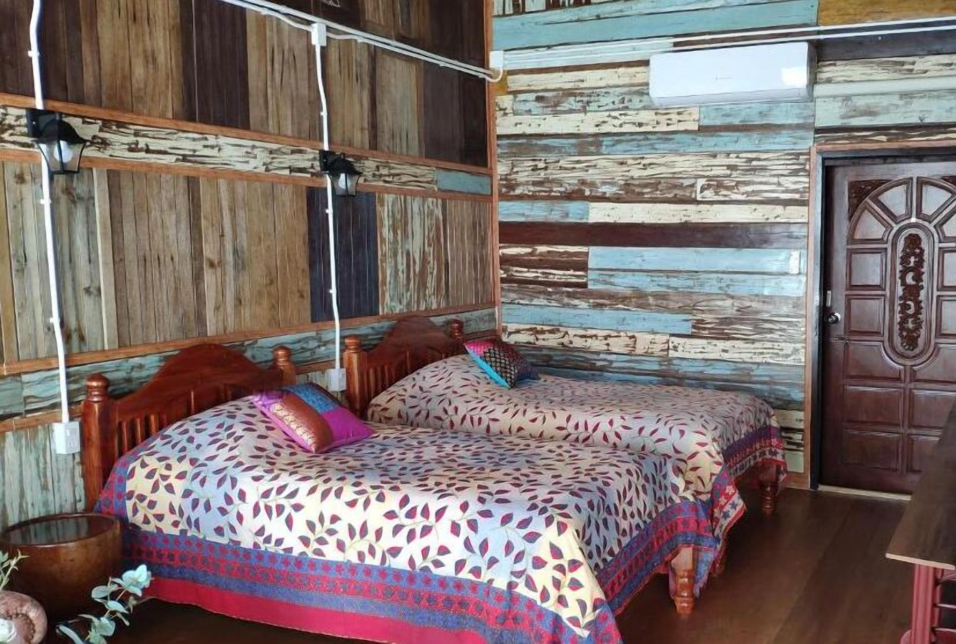 A room with two wooden beds with patterned bedding, a rustic wooden wall, and a wooden door.