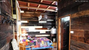 Una habitación rústica de madera con una cama, una silla, una mesita y una puerta.
