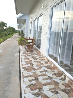 A covered outdoor area with a tiled floor, a wooden table, and chairs, adjacent to a building with large windows and a white exterior. - Coffee&Homestay568 Branch 2 (Muang Suang)