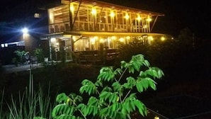 A two-story building with a glass facade and multiple windows, illuminated by warm interior lighting. - Coffee&Homestay568 Branch 2 (Muang Suang)