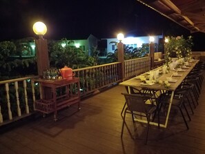 A long wooden deck with tables set for dining, surrounded by a wooden railing and illuminated by spherical lights. - Coffee&Homestay568 Branch 2 (Muang Suang)