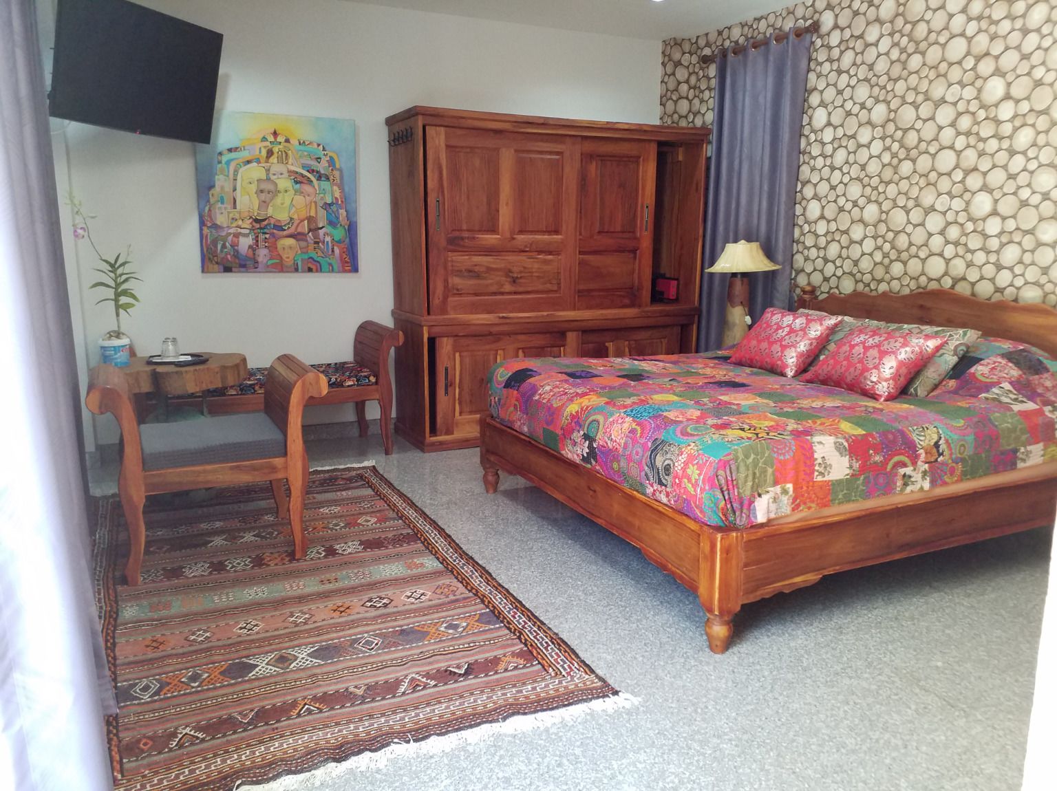 Une chambre à coucher avec un lit en bois, un bureau, une chaise, une armoire et un tapis à motifs.