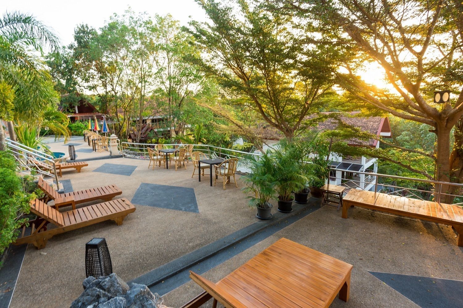 An outdoor patio area with wooden furniture, potted plants, and a view of a building in the background.