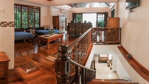 A spacious living area with a wooden staircase, a sofa, a coffee table, and a TV mounted on the wall. - Krabi Villa Phu Khao Private Resort (Krabi)