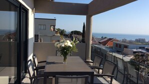 A balcony with a table and chairs, a vase of flowers, and a view of the sea and buildings. - 43 Ocean View Drive (Cape Town)