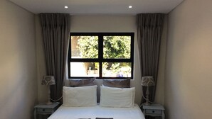 A neatly made bed with pillows and folded towels, two bedside tables with lamps, and a window with curtains. - 43 Ocean View Drive (Cape Town)