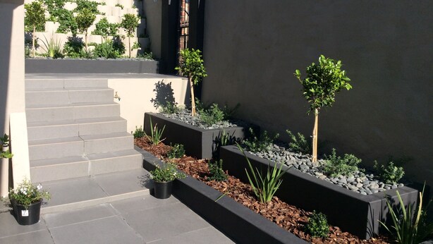 A modern outdoor staircase leading up to a building with a dark facade. There are potted plants and a small tree on the steps. - 43 Ocean View Drive (Cape Town)