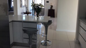 A modern kitchen with a central island, bar stools, and a vase of flowers. - 43 Ocean View Drive (Cape Town)