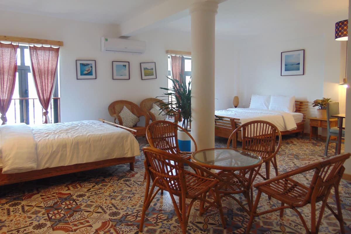 A hotel room with two beds, a dining table with chairs, a potted plant, and a window with curtains.