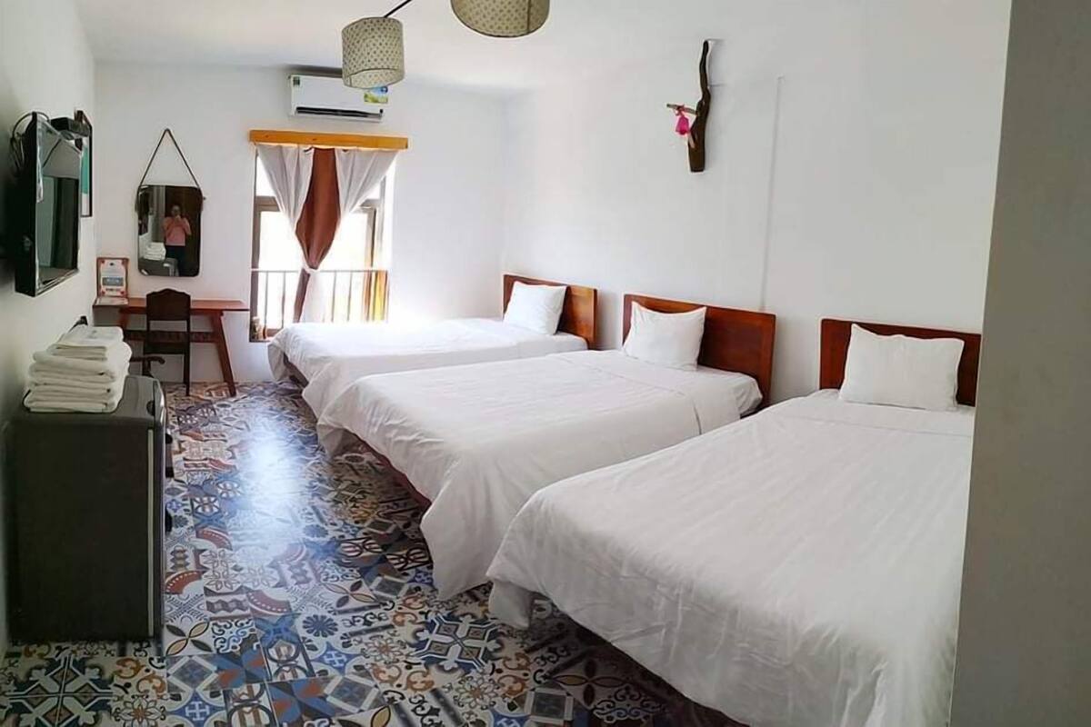 A hotel room with two single beds, a desk, a chair, and a patterned floor.