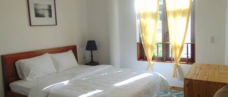 A bedroom with a bed, a bedside table with a lamp, a window with curtains, and a picture on the wall.