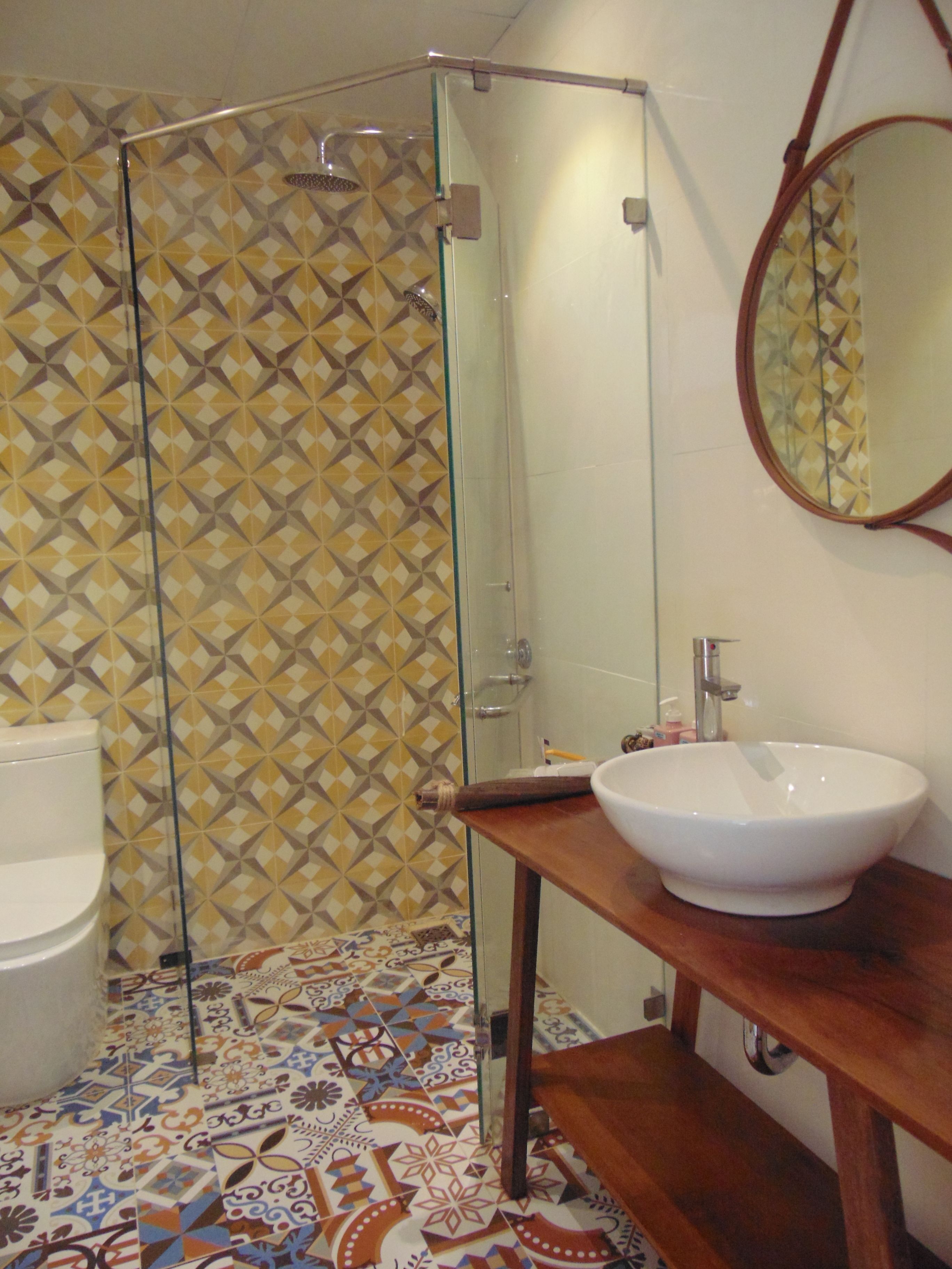 Un baño con cabina de ducha de vidrio, un lavabo blanco y baldosas de suelo estampadas.