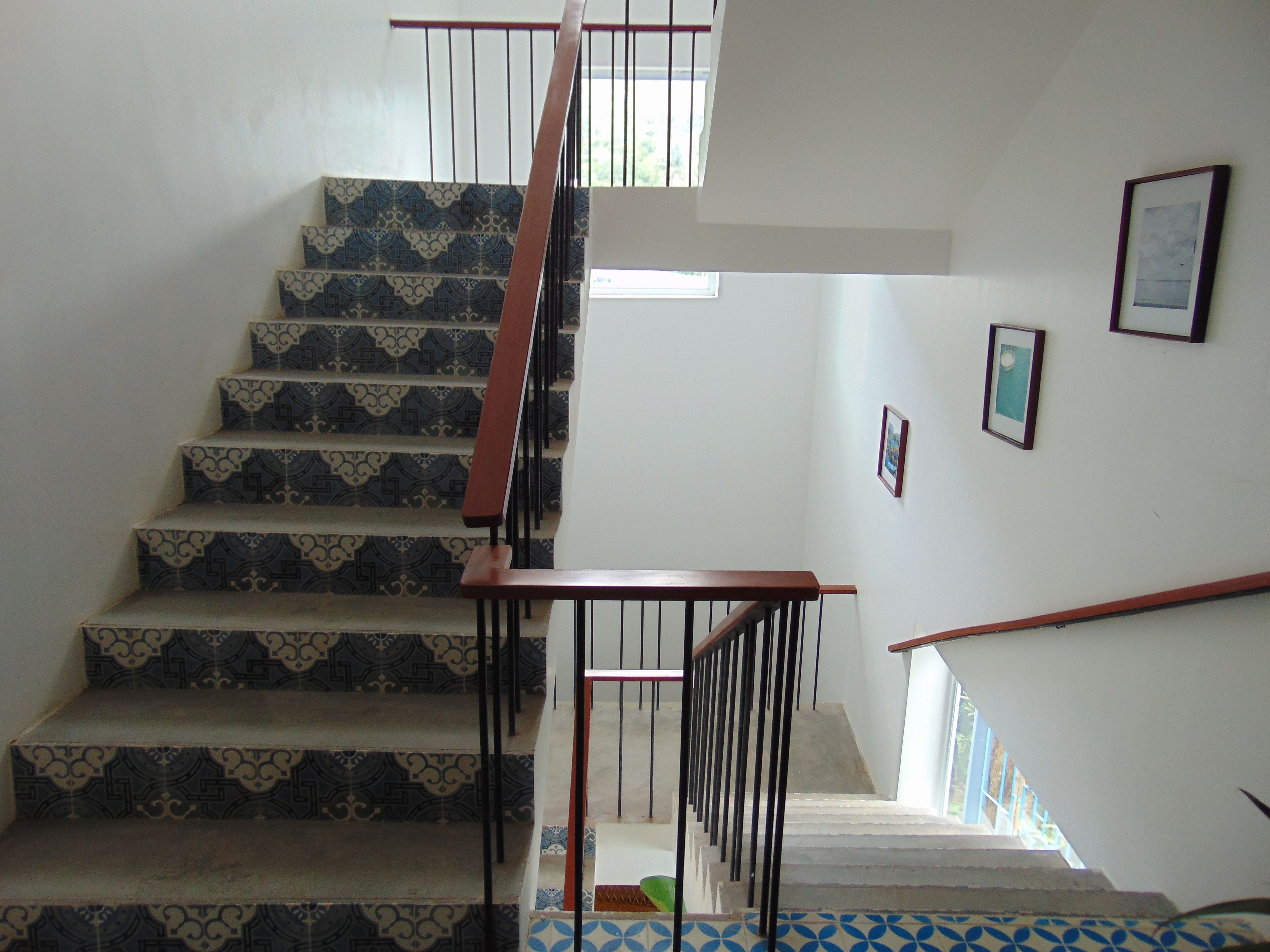 A staircase with patterned tiles, a wooden handrail, and metal railings.