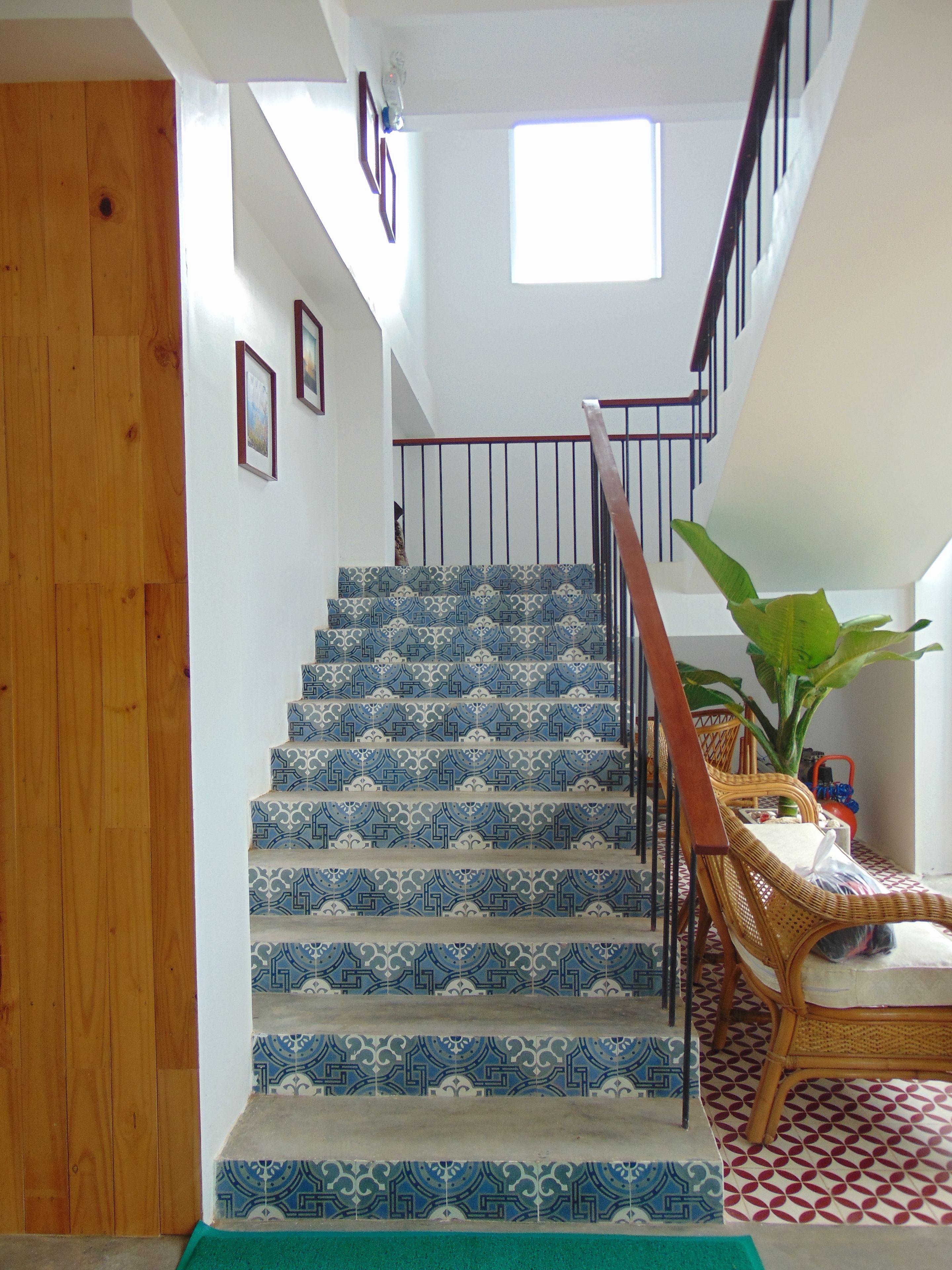 A staircase with patterned blue and white tiles, a wooden handrail, and a wicker chair with a cushion.