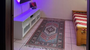 A room with a TV mounted on a white cabinet, a patterned rug on the floor, and a bed with a striped bedspread. - House / Villa - Giarre (Giarre)