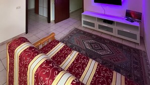 A living room with a TV on a white stand, a patterned sofa, a chandelier, and a door leading to another room. - House / Villa - Giarre (Giarre)
