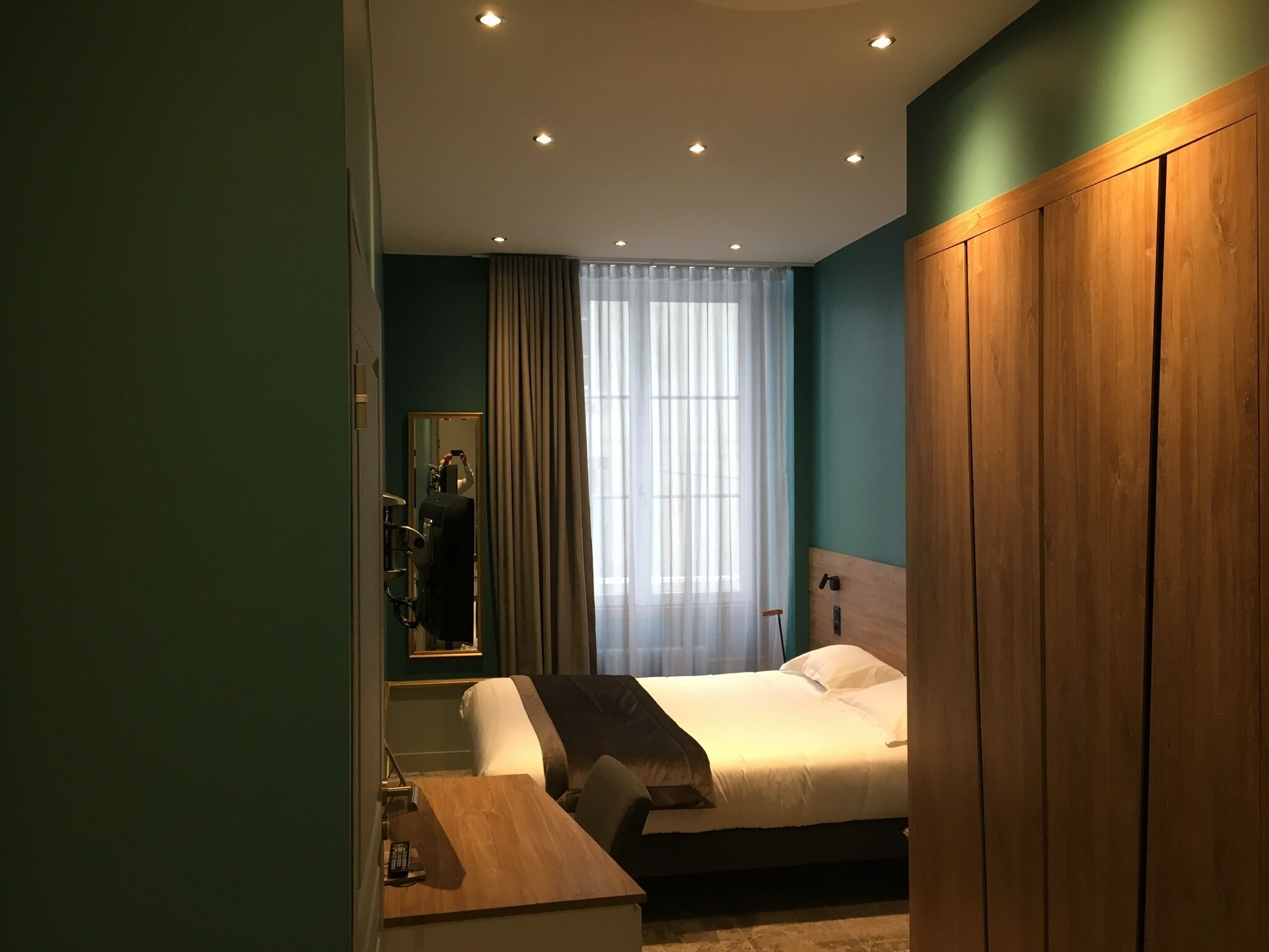 Een moderne hotelkamer met een groot bed, een houten garderobe, een nachtkastje en een spiegel.