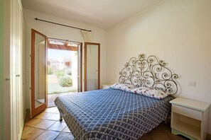 A bedroom with a bed, a nightstand, a window with curtains, and a view of the outside.
