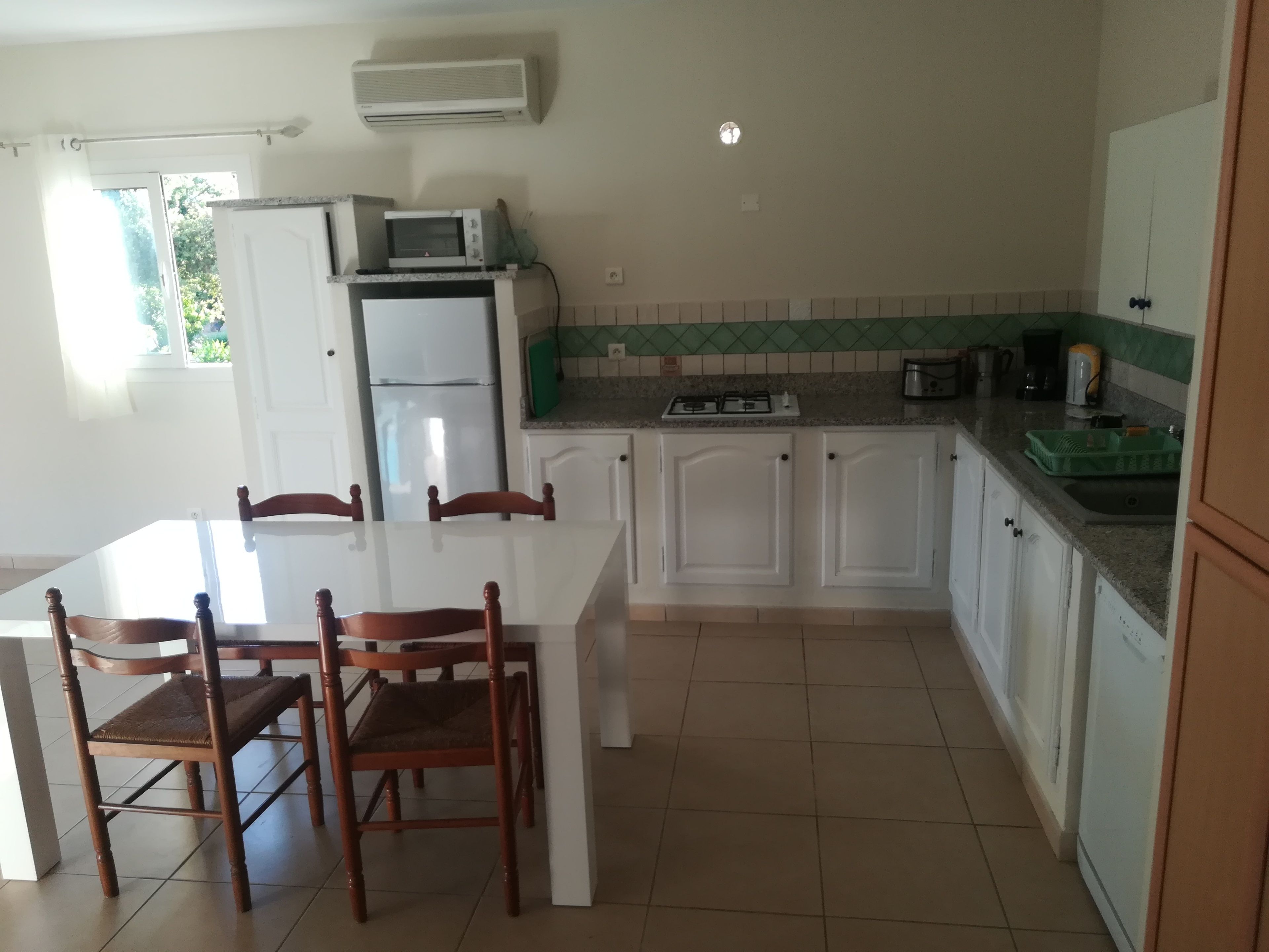 A kitchen with a white countertop, a built-in microwave, a stove, and a refrigerator. There are wooden chairs around a table.