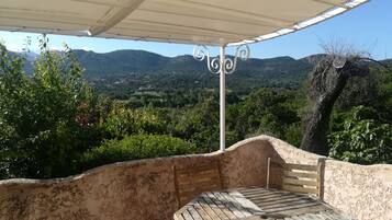 A covered outdoor seating area with a table and chairs, overlooking a mountainous landscape.