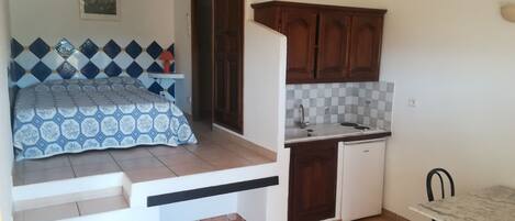 A compact room with a bed, a small kitchenette, and a dining area.