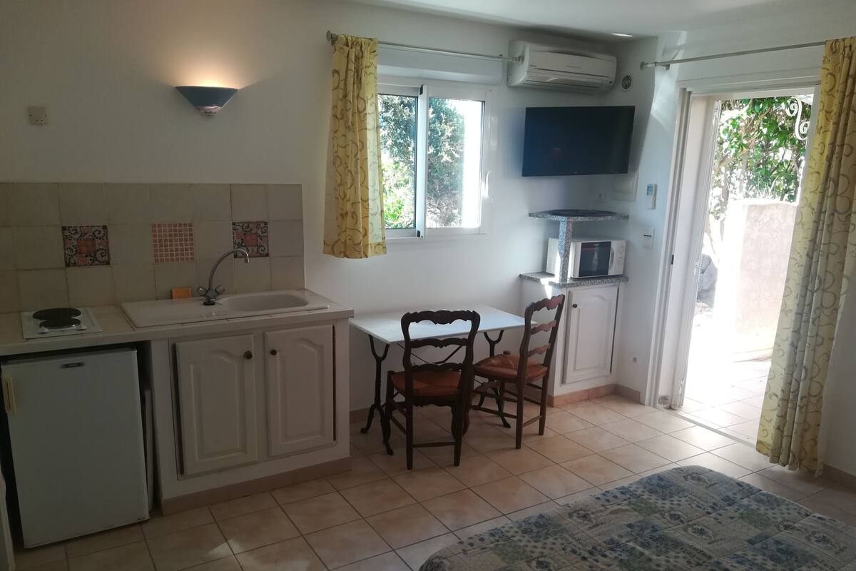 A compact kitchen with a dining area, a TV mounted above the microwave, and a sliding glass door leading to an outdoor area.