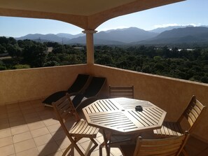 A balcony with a wooden table and chairs, offering a view of distant mountains and greenery. - Résidence Marina Di A Testa (Zonza)