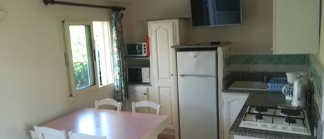 A compact kitchen with a dining table, chairs, a refrigerator, a microwave, a stove, and a window with curtains.