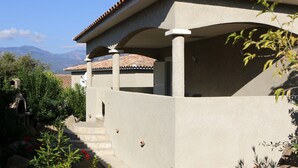 Un edificio con un porche cubierto, escalones que llevan a una puerta y una vista de montañas al fondo.