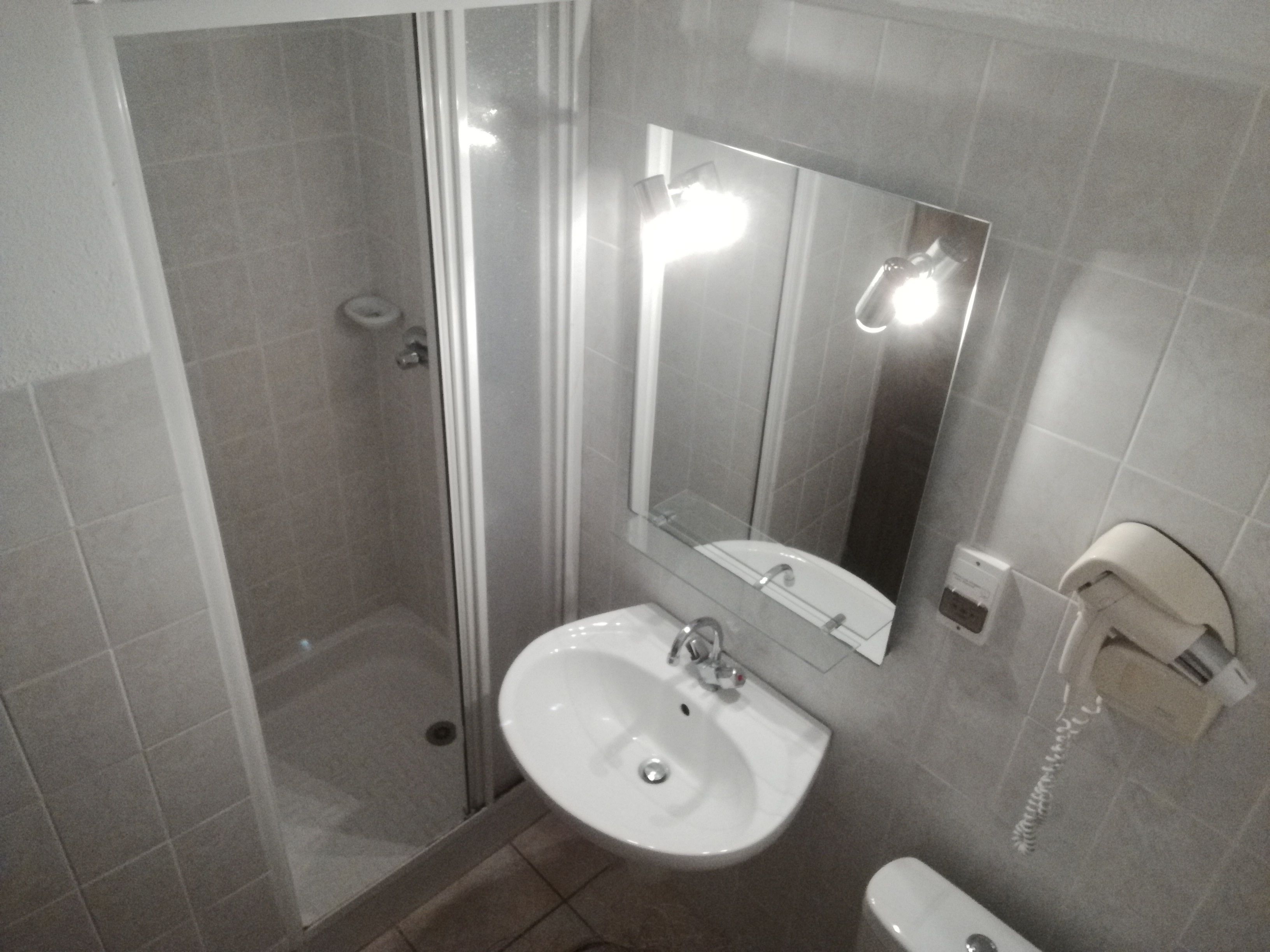 Une salle de bain avec une douche à parois de verre, un lavabo, un miroir et un sèche-mains.