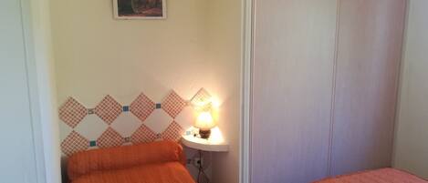 A bedroom with two beds, a nightstand with a lamp, a wall-mounted picture, and a wardrobe.