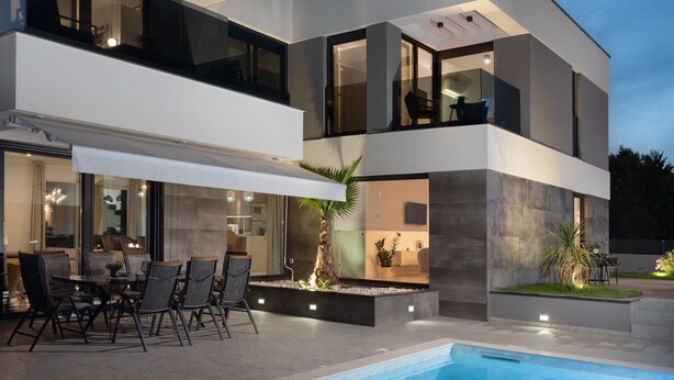 A modern two-story house with a pool, outdoor seating, and a well-lit interior. - Villa N Drage with pool  (Nin)