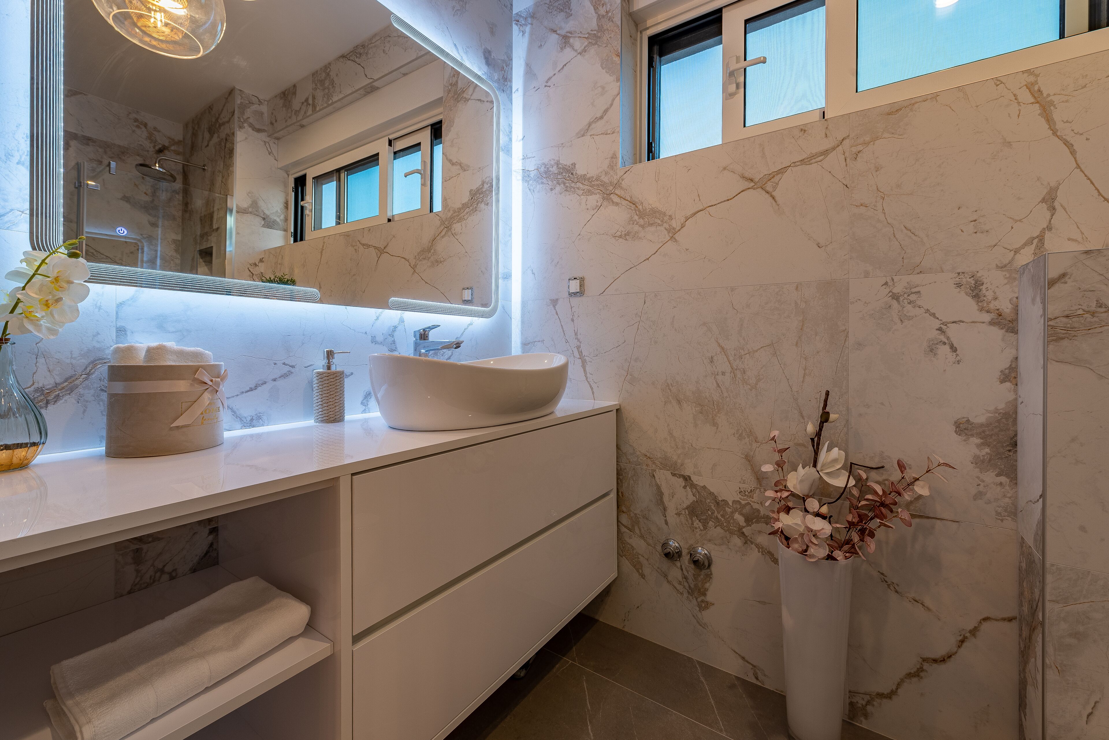A modern bathroom with a white vanity, a large mirror, and a vase with flowers.
