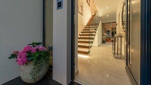A modern interior with a staircase leading to upper floors, a large potted plant with flowers, and a glass door entrance. - Villa N Drage with pool  (Nin)