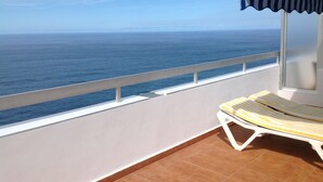A balcony with a view of the ocean, a striped sun lounger, and a striped awning.