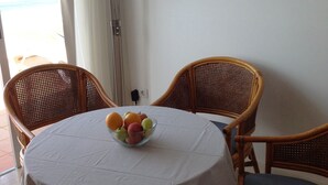 A round table with a white tablecloth, surrounded by wicker chairs. A bowl of fruit is placed on the table.
