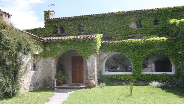 Un bâtiment en pierre avec un toit en tuiles, des murs couverts de lierre et une porte en bois située au centre.