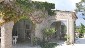 Un bâtiment en pierre doté d’une porte et de fenêtres en verre, un patio avec une table et des chaises, et des plantes en pot.