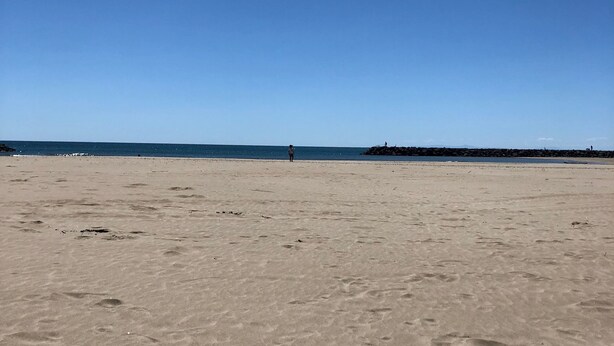 A wide sandy beach with footprints and a clear blue sky.
