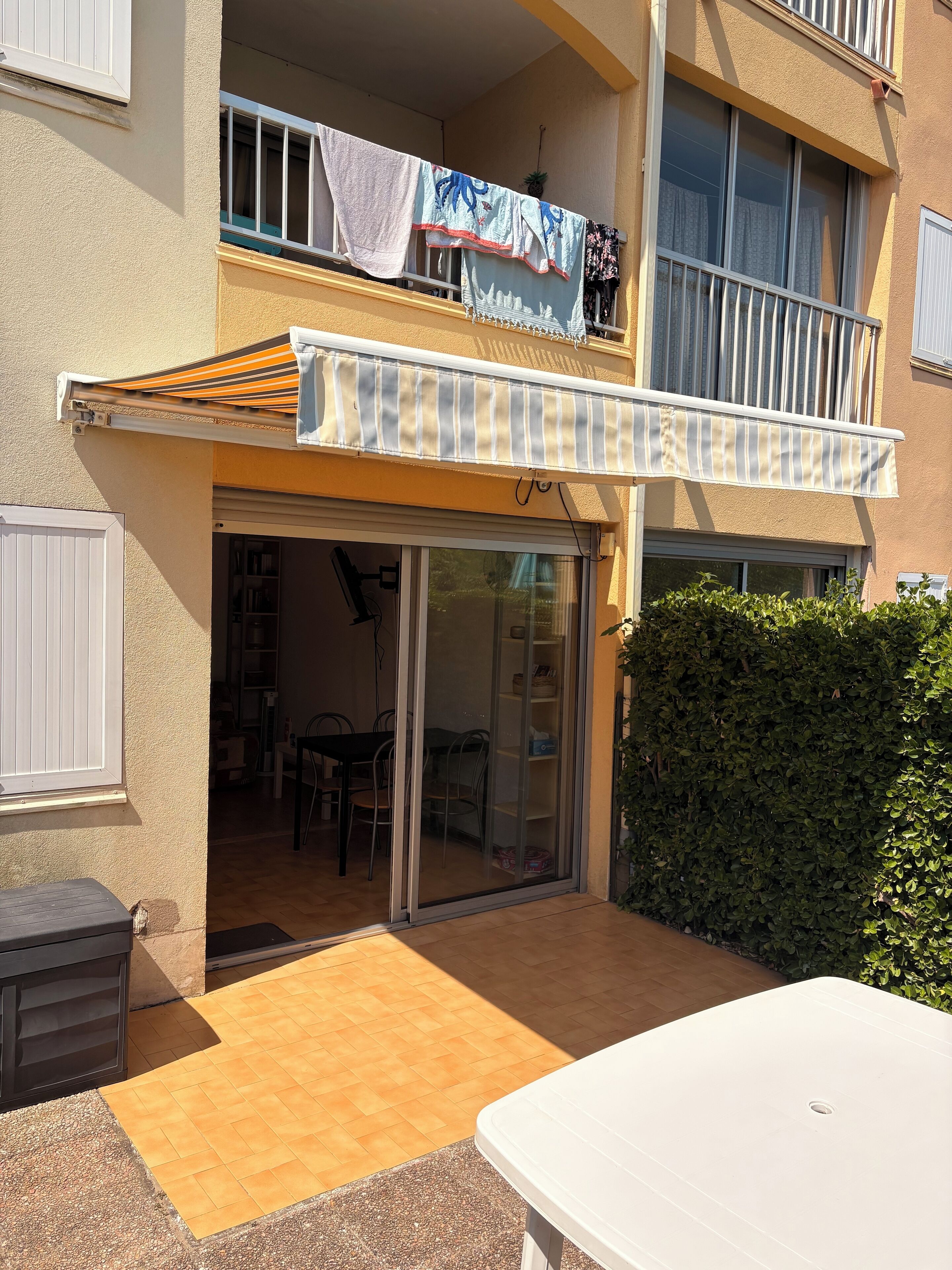 Un edifici residencial amb un balcó, una entrada amb porta corredissa de vidre i una petita zona d'estar a l'exterior.