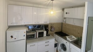 A compact kitchen with white cabinets, a microwave, a washing machine, and a sink.