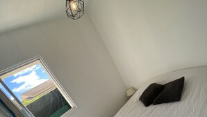 A bedroom with a bed, a window, and a hanging light fixture.
