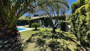 Un jardin bien entretenu, doté d’une piscine et bordé de différents arbres et arbustes.
